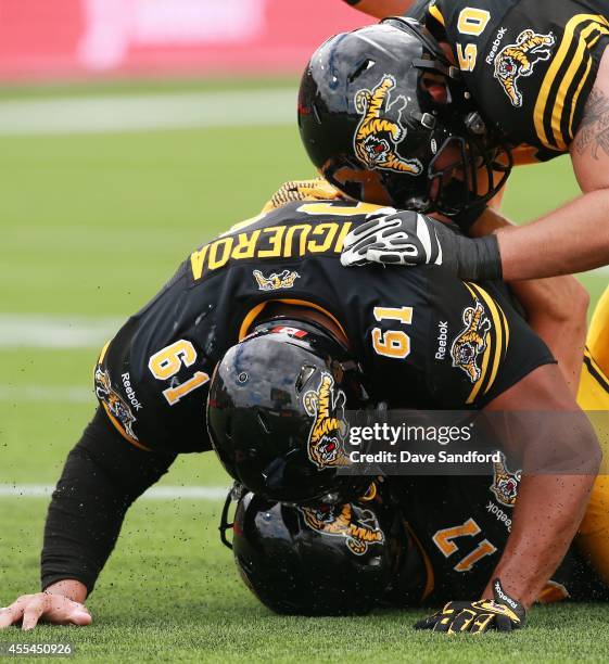 Luke Tasker of the Hamilton Tiger-Cats is jumped on by teammates Joel Figueroa Jake Olson after scoring his second touchdown of the game against the...