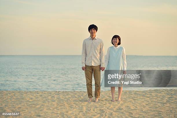 couple standing together on beach - asian man barefoot foto e immagini stock