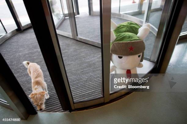 Dog walks through a revolving door as a plush toy of Mitu rabbit, the Xiaomi Corp. Mascot, stands on display at a Xiaomi Corp. Office in Beijing,...