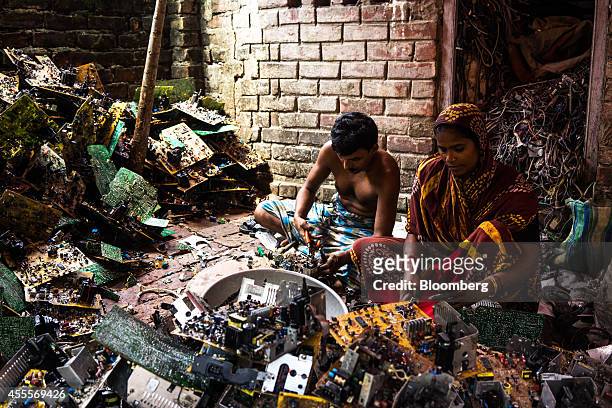 Man and a woman sit among piles of electronic waste as they dismantle computer peripherals at a family compound of houses in Sangrampur village, West...