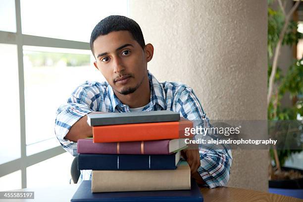 young student sitting at table with pile of books - puerto rican ethnicity stockfoto's en -beelden