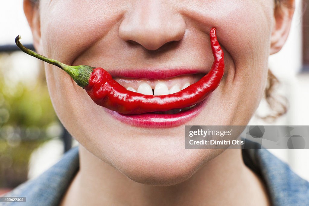 Young woman biting into red hot chilli