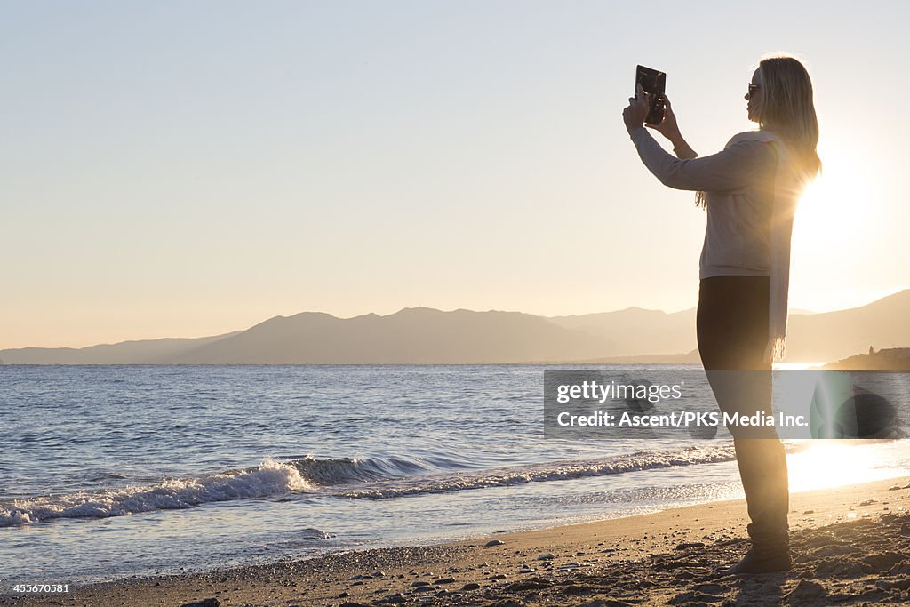 Woman takes picture with digital tablet, sea