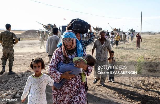 Syrian Kurds walk by Turkish soliders after crossing into Turkey near the southeastern town of Suruc in Sanliurfa province, on September 19, 2014....