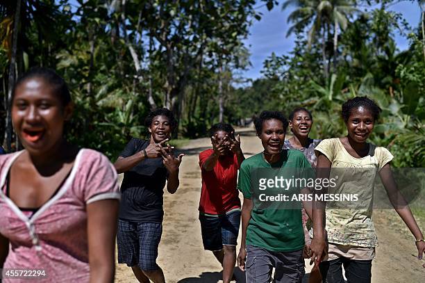 Young people smile and gesture while walking on a road near the village of Tora, in the jungle of Papua New Guinea, on September 9, 2014. AFP PHOTO /...