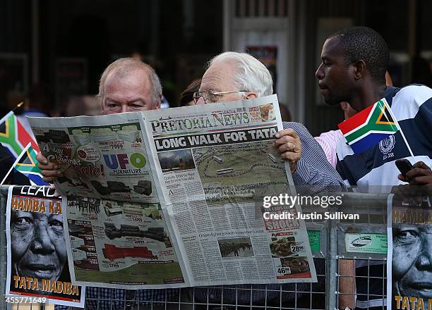 Spectators read the newspaper while waiting to see the funeral cortege of former South African president Nelson Mandela as it makes its way towards...