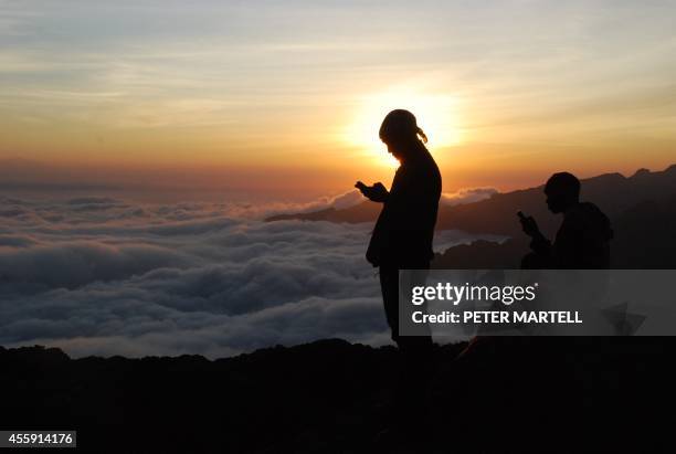 Tanzanian porters and guides stand on a rock half way up Kilimanjaro at sunset on September 21, 2014 trying to get a mobile phone signal to call...