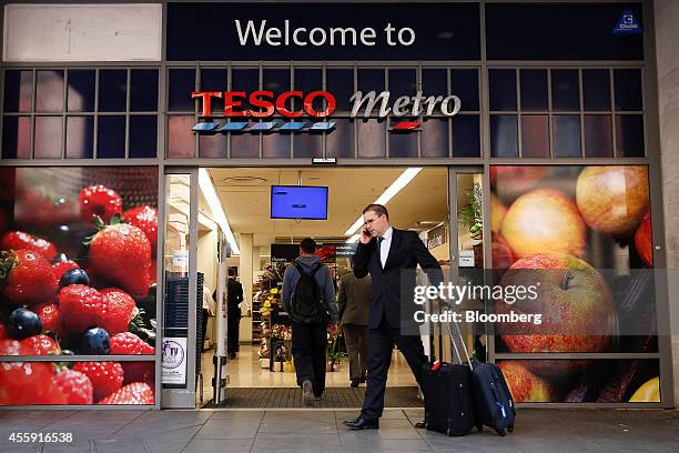 Man speaks on his mobile phone as he pulls his suitcases past the entrance to a Tesco Metro supermarket store, operated by Tesco Plc, in London,...