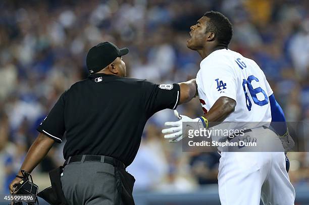 Yasiel Puig of the Los Angeles Dodgers is restrained by home plate umpire Adrian Johnson after Puig was hit by a pitch from Madison Bumgarner of the...