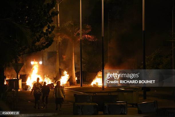 People walk past ignited barrages set up with garbages and wooden pallets through the road, on September 23, 2014 in Saint-Denis-de-la-Reunion....