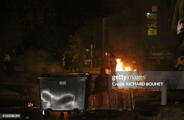 People stand next to an ignited barrage set up with garbages and wooden pallets through the road, on September 23, 2014 in Saint-Denis-de-la-Reunion....