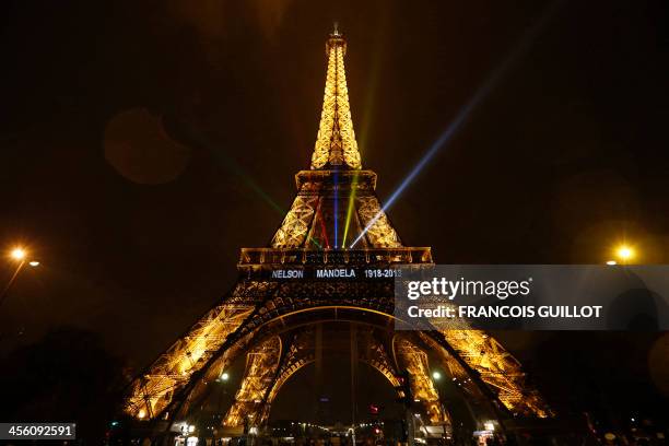 The words "Nelson Mandela, 1918 -2013" and light beams of colors of the South African national flag are seen on the illuminated Eiffel Tower on...