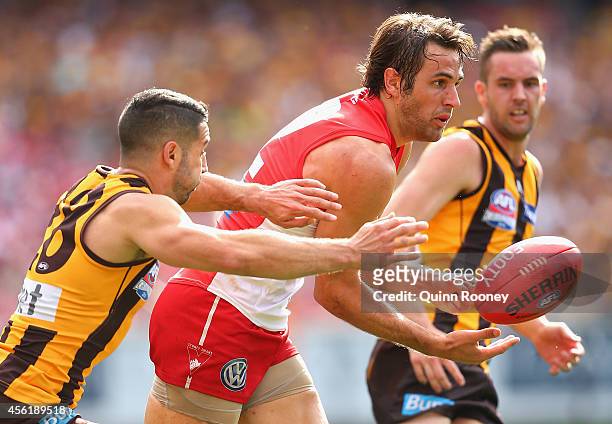 Josh Kennedy of the Swans handballs whilst being tackled by Paul Puopolo of the Hawks during the 2014 AFL Grand Final match between the Sydney Swans...