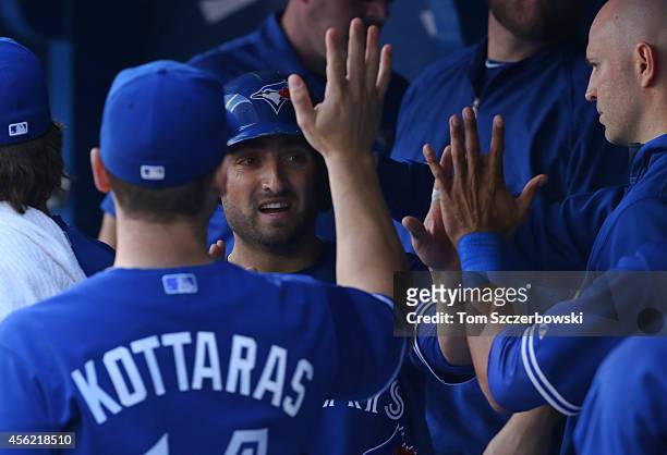 Kevin Pillar of the Toronto Blue Jays is congratulated by J.A. Happ and George Kottaras in the dugout after scoring a run in the third inning during...