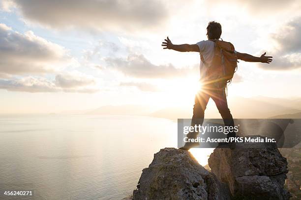 man stands between boulders on summit, arms out - hochgefühl stock-fotos und bilder
