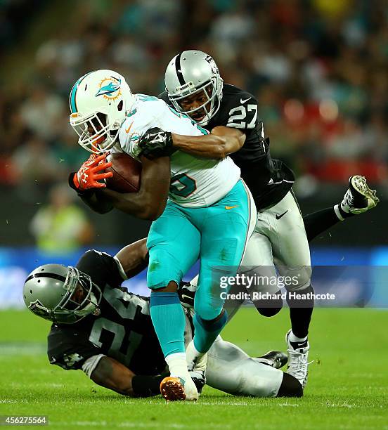 Lamar Miller of the Miami Dolphins is tackled by Charles Woodson of the Oakland Raiders and Carlos Rogers of the Oakland Raiders during the NFL match...