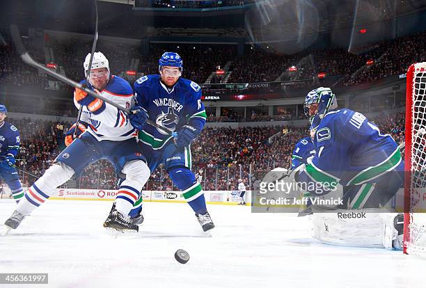 Yannick Weber of the Vancouver Canucks checks Jesse Joensuu of the Edmonton Oilers in front of Roberto Luongo of the Canucks during their NHL game at...