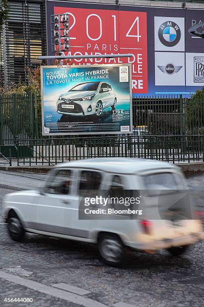 An automobile passes an advertisement for a Toyota Yaris hybrid automobile, manufactured by Toyota Motor Corp., near an exhibition hall branded with...
