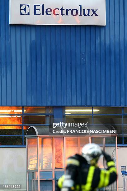 Firefighter walks past the logo of Swedish appliance maker Electrolux at its plant in Revin, eastern France, on October 1 whilst a fire burns during...