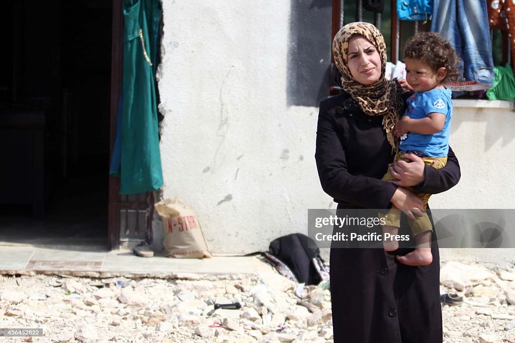 Palestinian woman stands in front of the house, which...