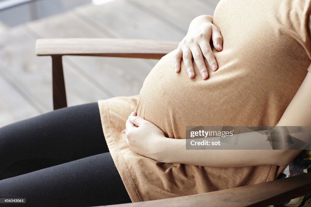 Pregnant woman touching abdomen sitting chair