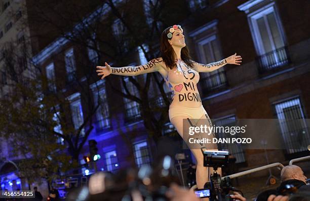 Thinly clad woman with messages written on her body stands on a fence near supporters of anticapitalist social movement Rodea El Congreso demonstrate...