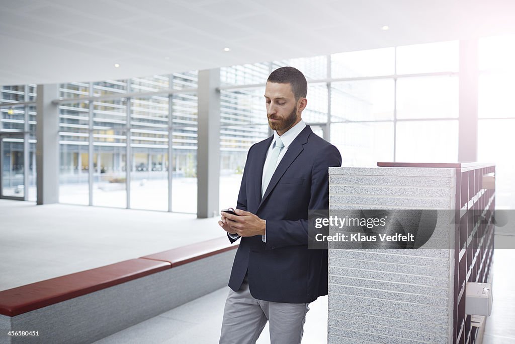 Creative businessman tjecking phone in hall