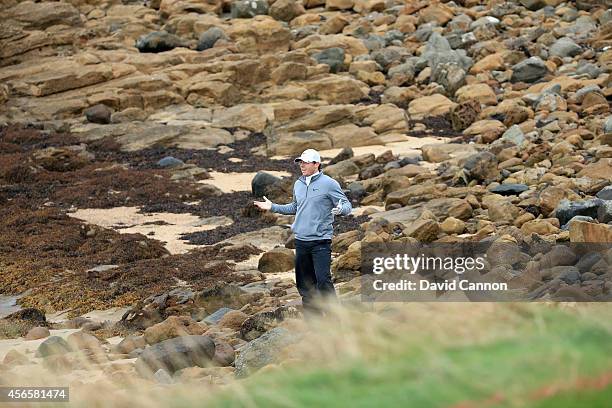 Rory McIlroy of Northern Ireland signals to his playing partner Ernie Els that he has found Els's ball on the rocks on the beach but it is unplayable...