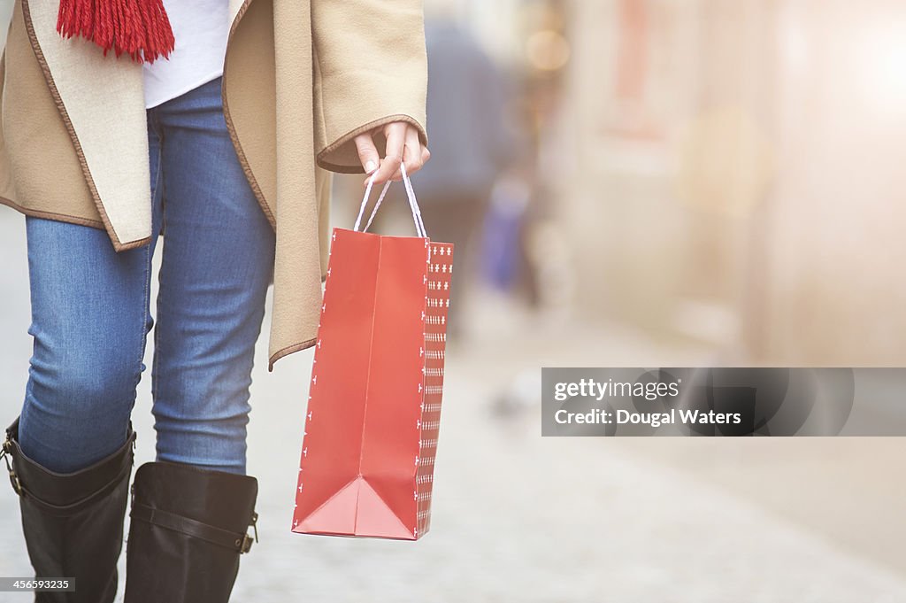 Woman walking in street with gift bag, close up.