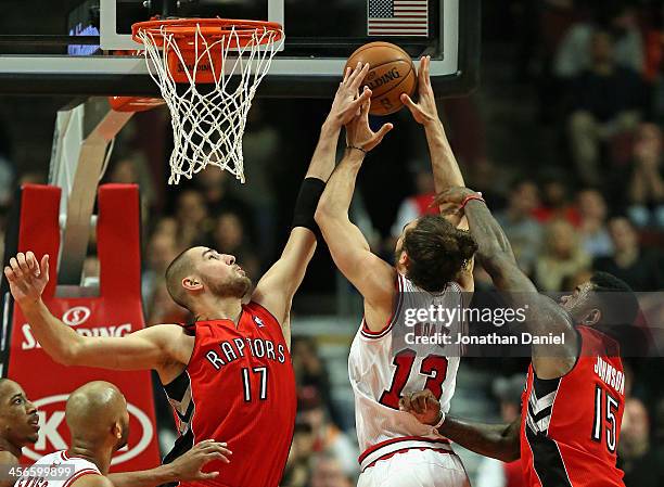 Jonas Valanciunas of the Toronto Raptors blocks a shot by Joakim Noah of the Chicago Bulls as Amir Johnson defends at the United Center on December...