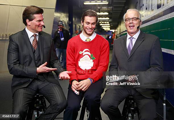 Eddie Lack of the Vancouver Canucks shows off his Christmas sweater while he is interviewed by Scott Oake and Craig Simpson of CBC after their NHL...