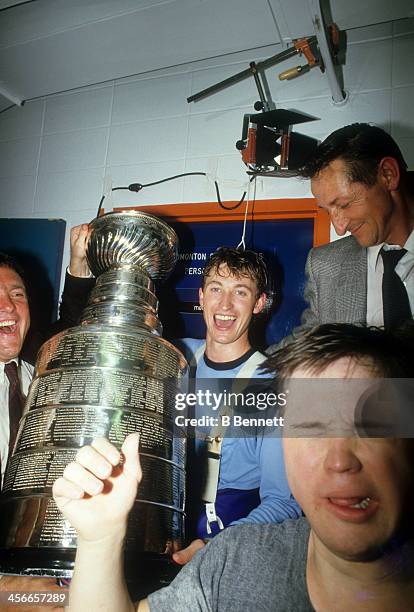 Wayne Gretzky of the Edmonton Oilers celebrates in the locker room with his father Walter Gretzky, Joey Moss and the Stanley Cup Trophy after the...