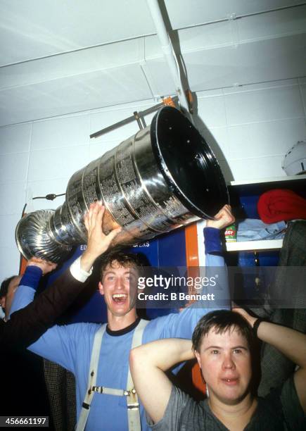 Wayne Gretzky of the Edmonton Oilers celebrates in the locker room with Joey Moss and the Stanley Cup Trophy after the Oilers defeated the...