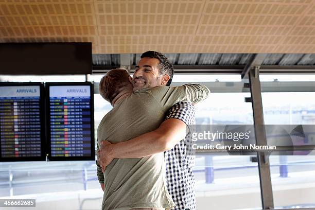 two gay men embracing at airport - fahrplan stock-fotos und bilder
