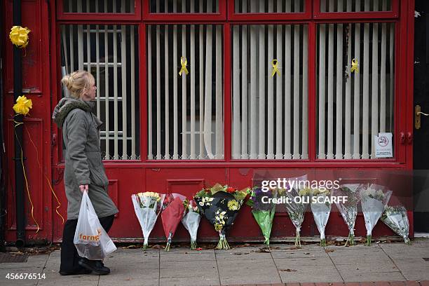 Yellow ribbons and a bouquet of flowers are seen, as a woman walks past the minicab office where murdered aid worker Alan Henning worked, in Eccles,...