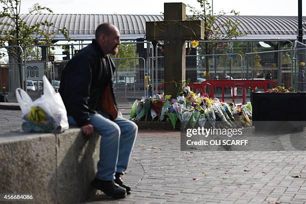 Man sits adjacent to the floral tributes at the base of the Eccles Cross for murdered aid worker Alan Henning in Eccles, north west England on...