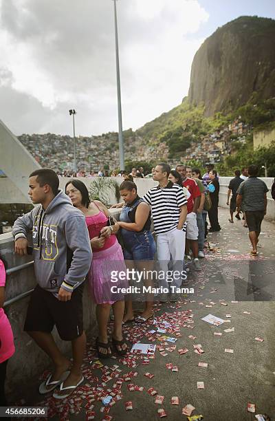 Brazilians wait in line to enter a polling station as campaign propaganda is scattered on the ground in the Rocinha favela, or community, on the day...