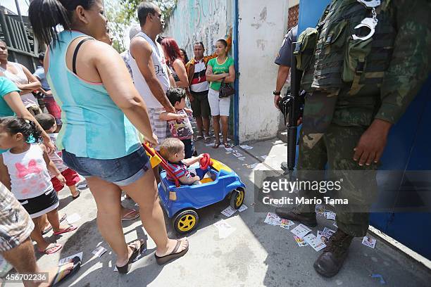 Brazilian soldier keeps watch as people with children wait to enter a polling station in the Complexo da Mare favela, or community, on the day of...