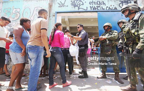 Brazilian soldiers keep watch as people wait to enter a polling station in the Complexo da Mare favela, or community, on the day of national...