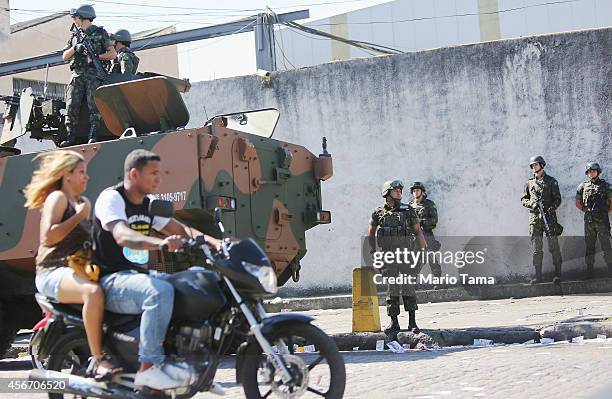 People drive past as Brazilian soldiers keep watch in the Complexo da Mare favela, or community, on the day of national elections on October 5, 2014...