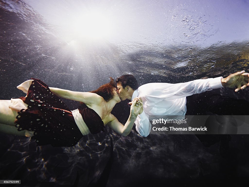 Underwater view of couple holding hands kissing