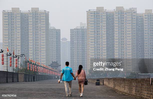Young couple walk along the old Xi'an city wall, in front of them is a huge residential housing block. According to the housing index issued in Sept,...