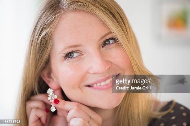 woman putting on earring, smiling - boucle d'oreille photos et images de collection