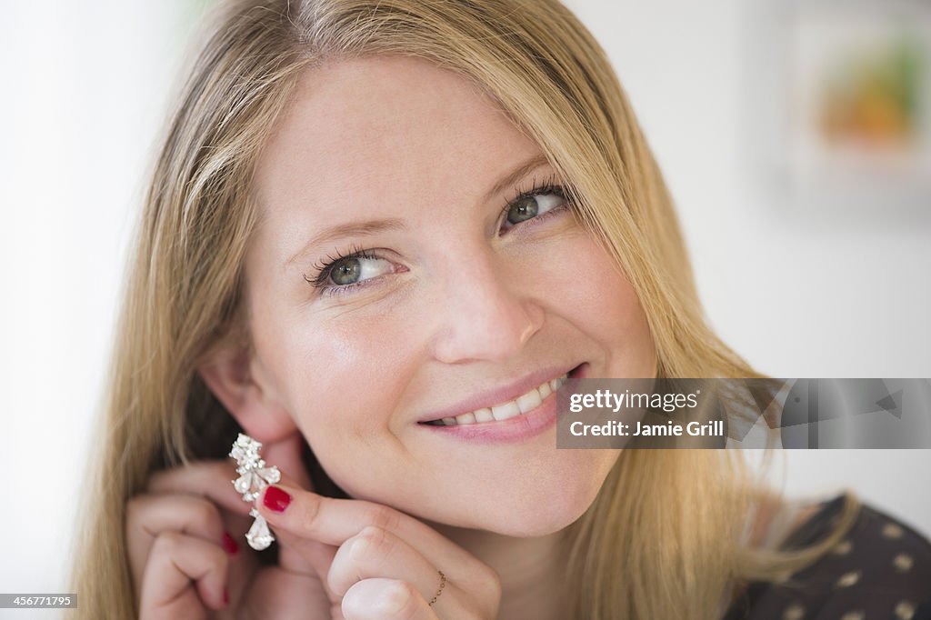 Woman putting on earring, smiling