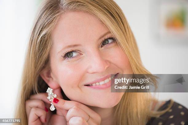 woman putting on earring, smiling - ear piercing stock pictures, royalty-free photos & images