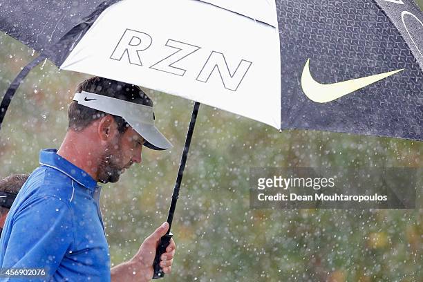 Scott Jamieson of Scotland shelters from the rain under his umbrella after he hits his tee shot on the 1st hole during Day 1 of the Portugal Masters...