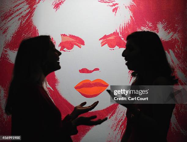 Employees pose next to a painting by Andy Warhol entitled 'Brigitte Bardot' during a press preview at Sotheby's on October 10, 2014 in London,...