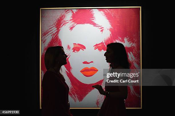 Employees pose next to a painting by Andy Warhol entitled 'Brigitte Bardot' during a press preview at Sotheby's on October 10, 2014 in London,...