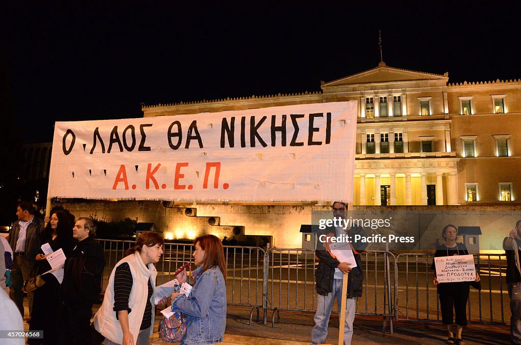 A banner is held in front of the Greek Parliament that reads...