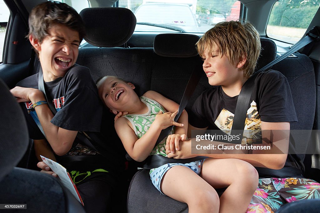 3 boys playing in the back seat of a car